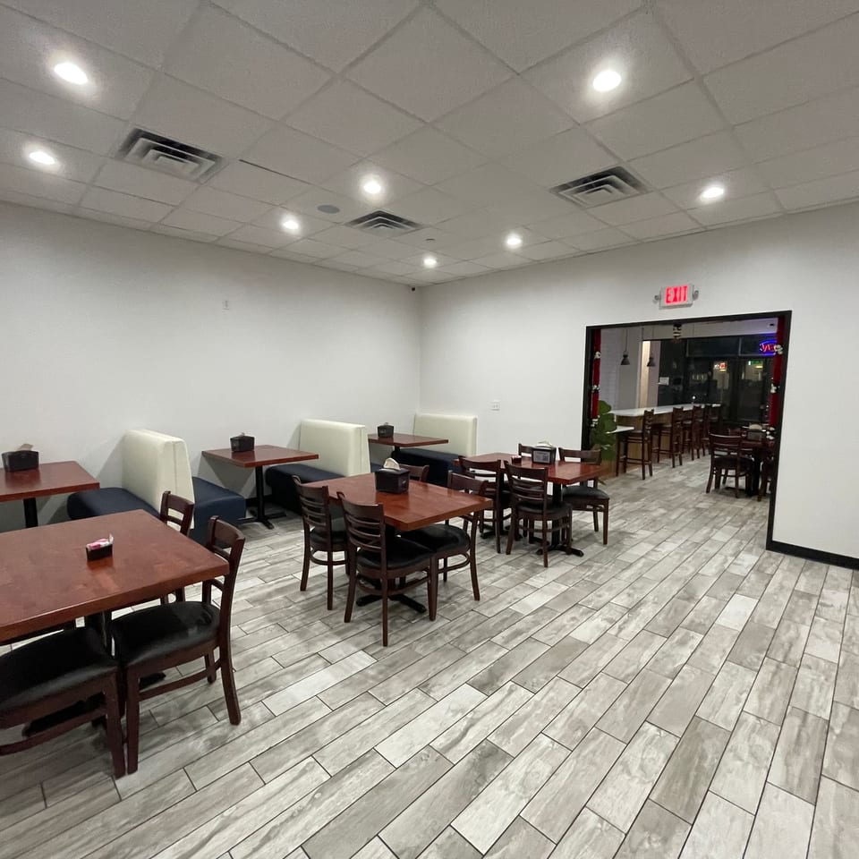 This is a wide shot of a clean, brightly lit restaurant dining area featuring wooden tables, dark upholstered chairs, and booth seating on a light-colored wood-look floor.